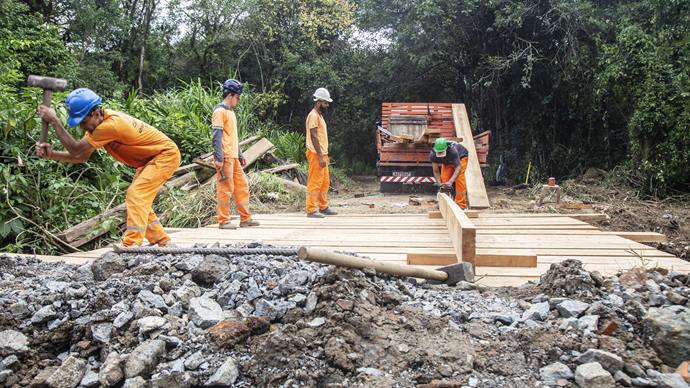 Equipes do Departamento de Pontes e Drenagem da Secretaria Municipal de Obras Públicas (Smop) trabalhando na reconstrução da ponte de madeira sobre o Rio Passaúna, na Rua Leonardo Kubis, no bairro Orl